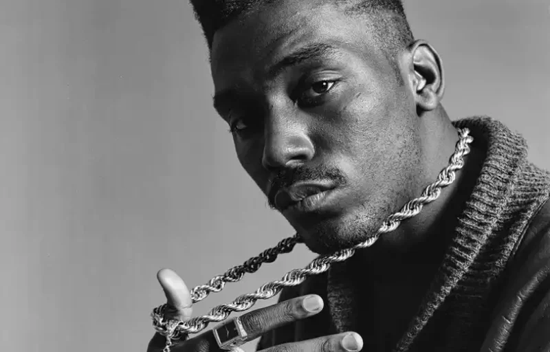 Black-and-white portrait of Big Daddy Kane holding a twisted chain necklace, emphasizing his iconic high-top fade and serious expression in hip-hop visual storytelling.